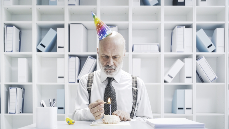 a business man lighting the candle of his birthday cake on his own and in the office