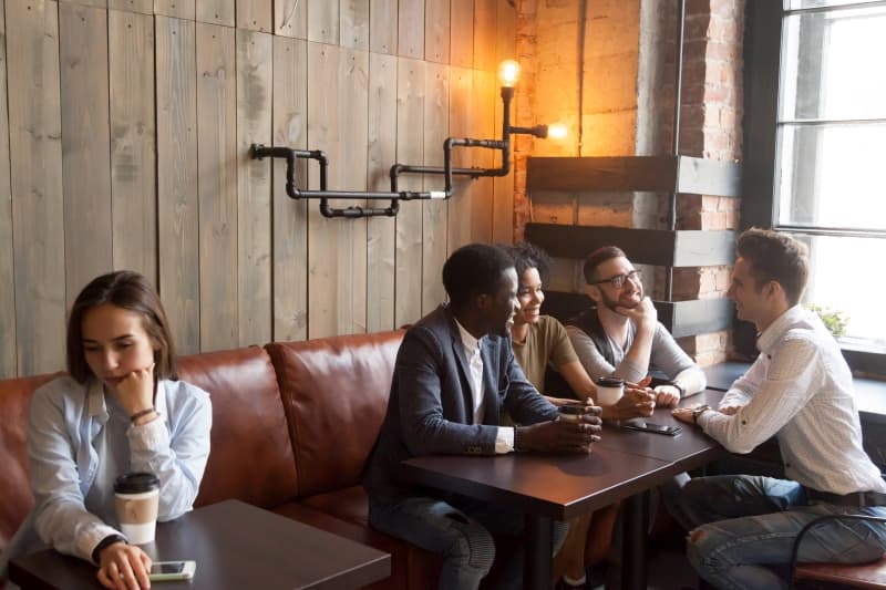 woman sitting on her own while friends chat on another table